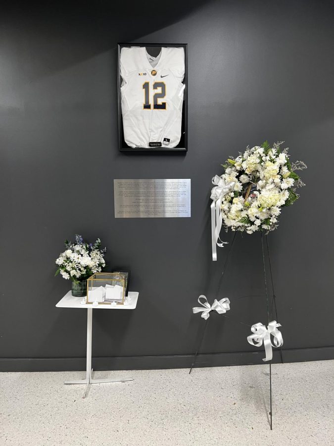 Danroy DJ Henrys football jersey hangs on the wall across from the Student Center in One Pace Plaza with a new plaque. A box of notes sits on the table, written at DJs Candlelight Vigil on Oct. 24 from students and faculty to reflect and remember those who have died at the hands of police brutality. (Photo/Mandi Karpo)
